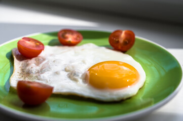 A freshly cooked hot fried egg and cherry tomatoes cut in half lie on a green plate. Healthy breakfast. Close-up.