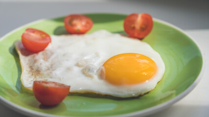 A freshly cooked hot fried egg and cherry tomatoes cut in half lie on a green plate. Healthy breakfast. Close-up.