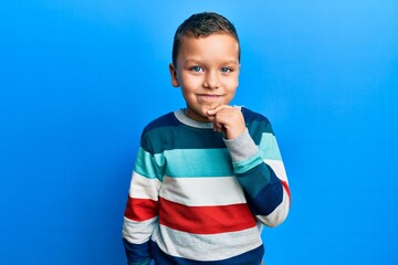 Little kid boy wearing striped sweater smiling looking confident at the camera with crossed arms and hand on chin. thinking positive.