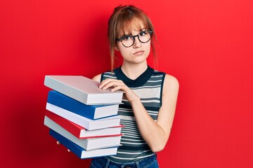 Redhead young woman holding a pile of books skeptic and nervous, frowning upset because of problem. negative person.