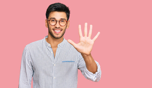 Young handsome man wearing casual clothes and glasses showing and pointing up with fingers number five while smiling confident and happy.