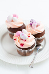 Three Easter chocolate cupcakes with caramel filling and decoration of small Easter eggs from marzipan on a white porcelain plate. Selective focus