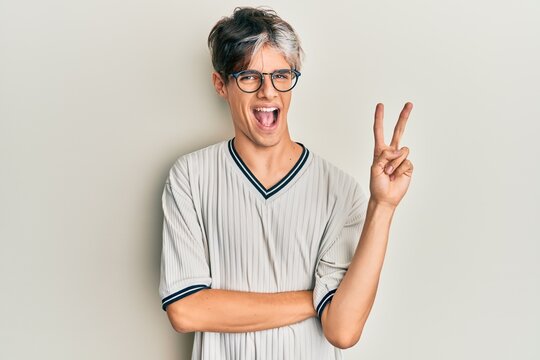 Young hispanic man wearing casual clothes and glasses smiling with happy face winking at the camera doing victory sign. number two.