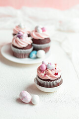 Three Easter chocolate cupcakes with caramel filling and decoration of small Easter eggs from marzipan on a white porcelain plate. Selective focus