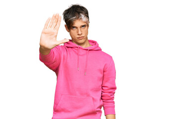 Young hispanic man wearing casual pink sweatshirt doing stop sing with palm of the hand. warning...