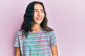 Fototapeta premium Hispanic teenager girl with dental braces wearing casual clothes looking away to side with smile on face, natural expression. laughing confident.