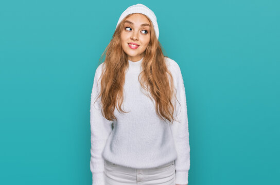 Young caucasian girl wearing wool sweater and winter cap smiling looking to the side and staring away thinking.