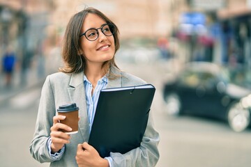 Young hispanic businesswoman drinking coffee holding binder at the city.