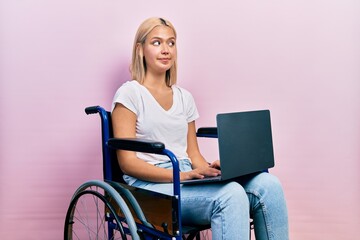 Obraz na płótnie Canvas Beautiful blonde woman sitting on wheelchair holding laptop smiling looking to the side and staring away thinking.