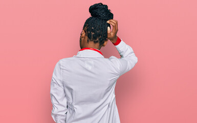 Young african american woman wearing doctor uniform and stethoscope backwards thinking about doubt with hand on head