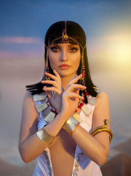 Portrait of Egypt Style woman. Sexy girl goddess Queen Cleopatra stand in desert pyramids. Art ancient pharaoh costume white dress gold accessories. Egyptian makeup. Creative headband, snake bracelet.