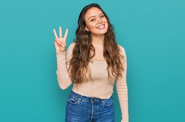 Fototapeta premium Young hispanic girl wearing casual clothes showing and pointing up with fingers number three while smiling confident and happy.