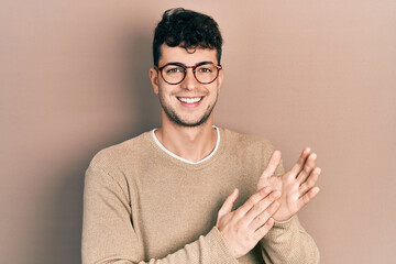 Young hispanic man wearing casual clothes and glasses clapping and applauding happy and joyful, smiling proud hands together