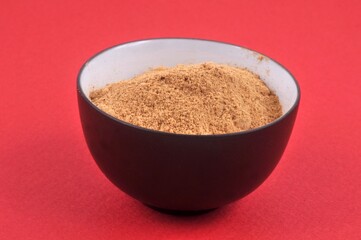 Gingembre en poudre dans un ramequin en gros plan sur fond rouge