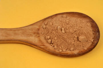 Gingembre en poudre dans une cuillère en bois en gros plan sur fond jaune