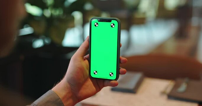 Unrecognizable person using a smartphone with green chroma key screen in cafe. Hands on phone with mockup display in restaurant - always online 4k footage