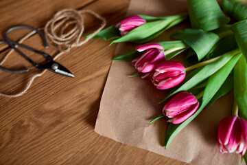 Fototapeta na wymiar Floristic workplace with craft paper, twine Arranging pink tulips bouquet on wooden table