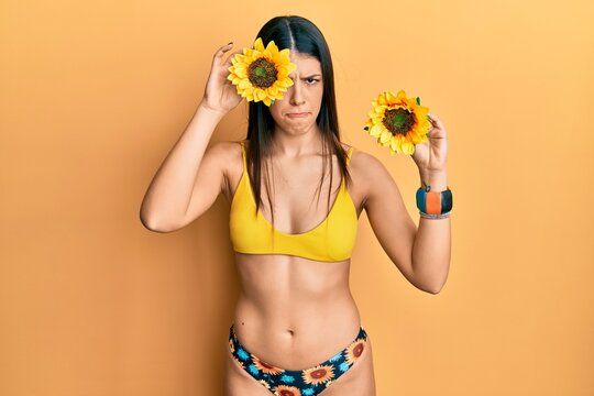 Young hispanic woman wearing bikini holding sunflowers skeptic and nervous, frowning upset because of problem. negative person.