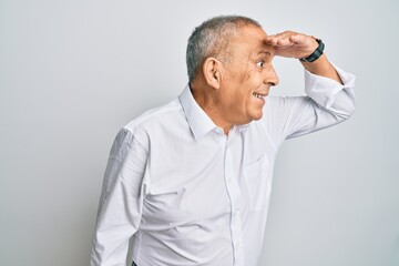 Handsome senior man wearing casual white shirt very happy and smiling looking far away with hand over head. searching concept.