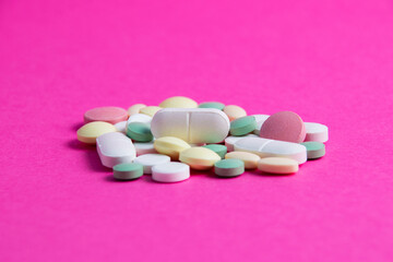 Many multicolored vitamins and pills on a pink background copy space, close-up