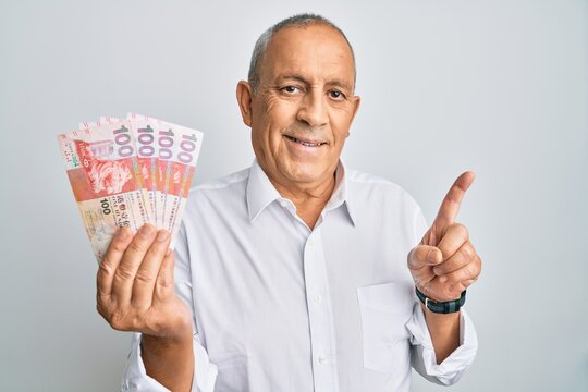 Handsome senior man holding 100 hong kong dollars banknotes smiling happy pointing with hand and finger to the side