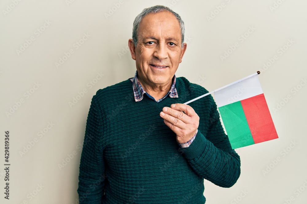 Poster handsome senior man with grey hair holding madagascar flag looking positive and happy standing and s