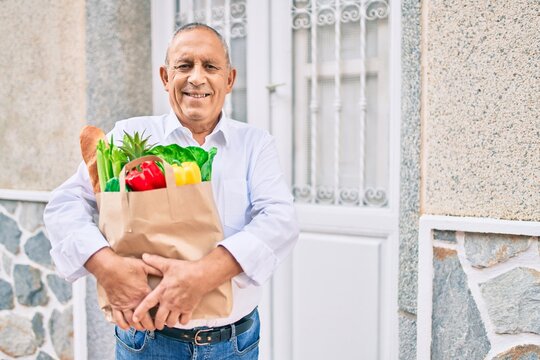 Senior man smiling happy holding paper bag with food walking at the city.