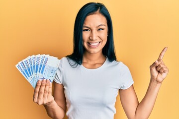 Beautiful hispanic woman holding 1000 south korean won banknotes smiling happy pointing with hand and finger to the side