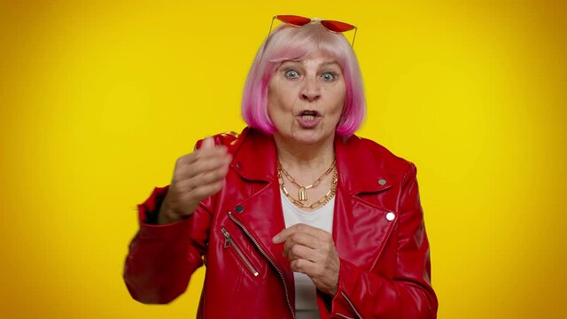 Get out of here. You are fired. Senior old granny rocker woman with pink hair pointing finger away asking to leave him alone strict boss firing, conflict. Yellow background. Elderly emo grandmother