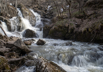 Waterfall in Bashkortostan in early spring. A stormy stream of water among large stones.