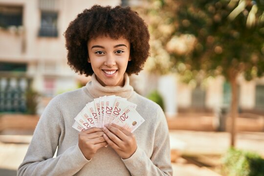 Young hispanic girl smiling happy holding israel shekels at the city.