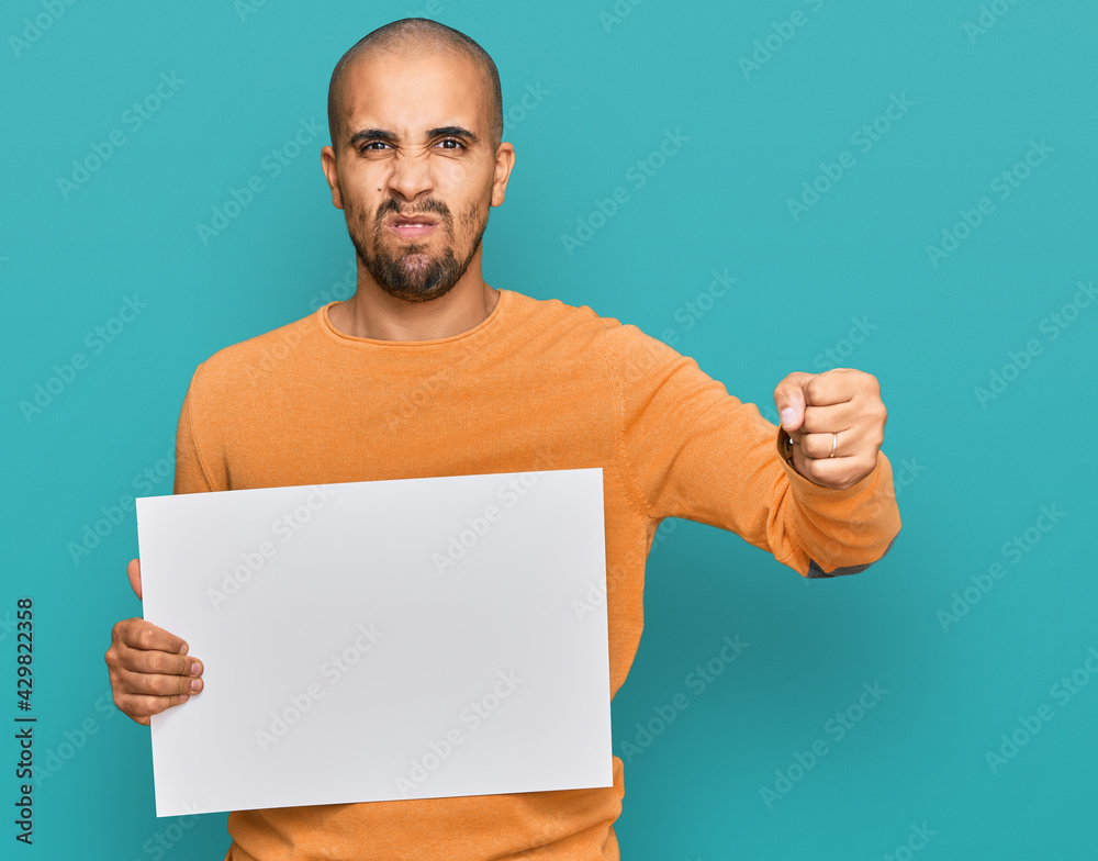 Sticker hispanic adult man holding blank empty banner annoyed and frustrated shouting with anger, yelling cr