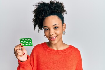 Young african american girl holding birth control pills looking positive and happy standing and...