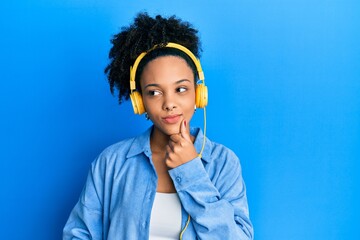 Young african american girl listening to music using headphones serious face thinking about question with hand on chin, thoughtful about confusing idea