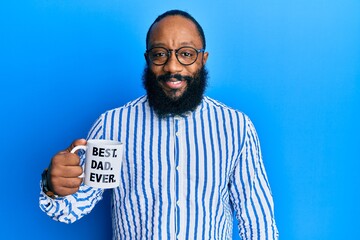 Young african american man drinking mug of coffe with best dad ever message looking positive and happy standing and smiling with a confident smile showing teeth