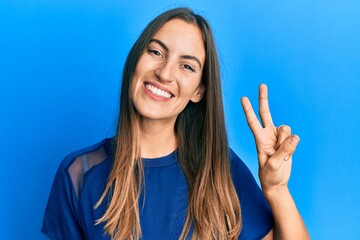 Fototapeta premium Young beautiful woman wearing casual clothes smiling with happy face winking at the camera doing victory sign. number two.