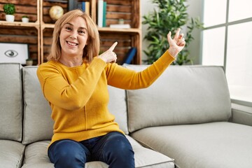 Obraz premium Middle age caucasian woman wearing casual clothes sitting on the sofa at home smiling and looking at the camera pointing with two hands and fingers to the side.