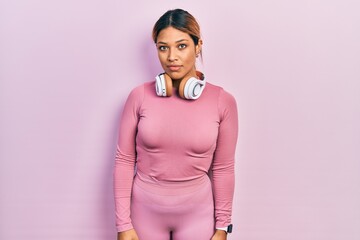 Obraz premium Beautiful hispanic woman wearing gym clothes and using headphones relaxed with serious expression on face. simple and natural looking at the camera.