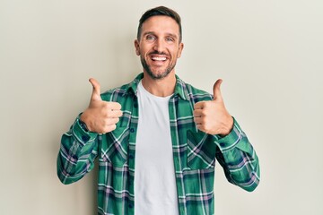 Handsome man with beard wearing casual clothes success sign doing positive gesture with hand, thumbs up smiling and happy. cheerful expression and winner gesture.