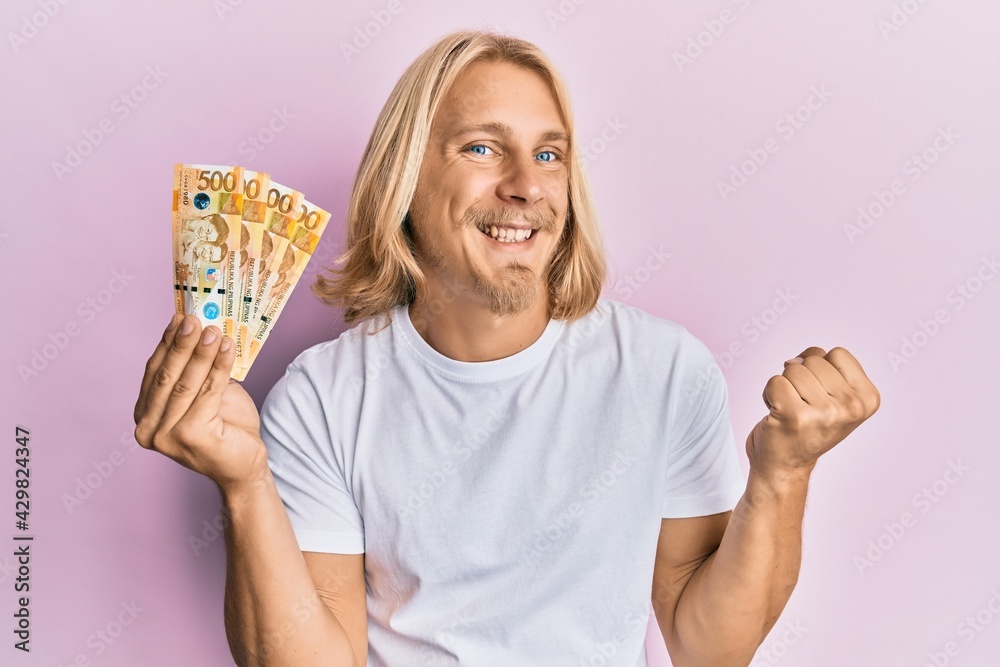 Sticker caucasian young man with long hair holding 500 philippine peso banknotes screaming proud, celebratin