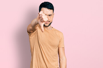 Fototapeta premium Hispanic man with beard wearing casual t shirt looking unhappy and angry showing rejection and negative with thumbs down gesture. bad expression.
