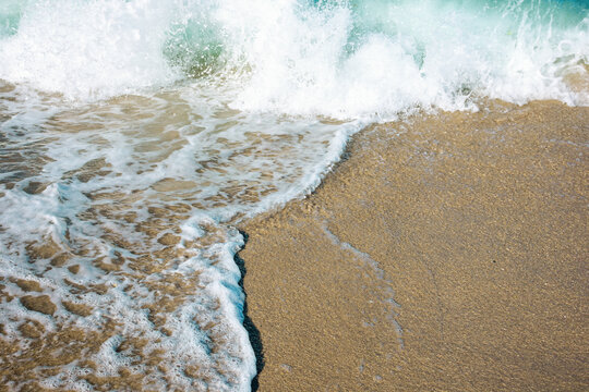 close up texture of the sea wave rolling on to the golden sandy beach. abstract nature background on a sunny summer day