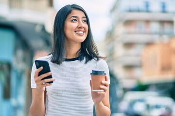 Young hispanic woman smiling happy using smartphone and drinking take away coffee at the city.