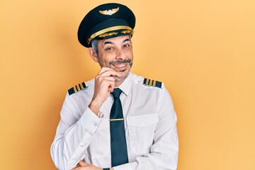 Handsome middle age man with grey hair wearing airplane pilot uniform looking confident at the...