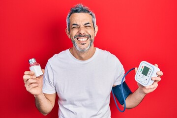 Handsome middle age man with grey hair using blood pressure monitor holding salt smiling and...