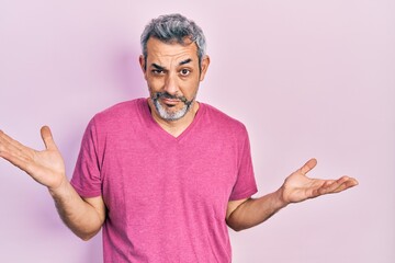 Handsome middle age man with grey hair wearing casual pink t shirt clueless and confused with open arms, no idea and doubtful face.