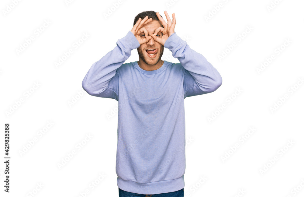 Poster young caucasian man wearing casual clothes doing ok gesture like binoculars sticking tongue out, eye