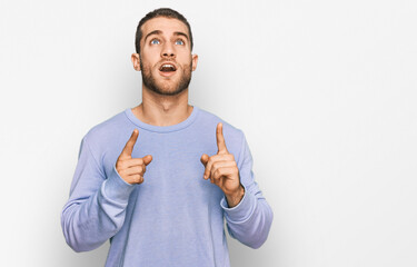 Young caucasian man wearing casual clothes amazed and surprised looking up and pointing with fingers and raised arms.