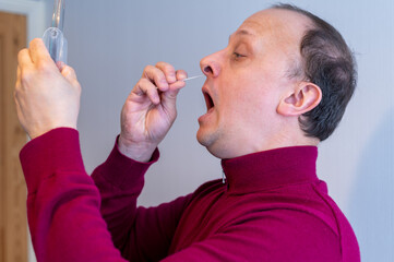 Man using a Covid-19 Rapid Lateral Flow Test swab in his nostril whilst looking in a hand held mirror