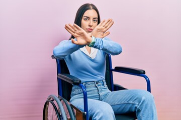 Beautiful woman with blue eyes sitting on wheelchair rejection expression crossing arms doing...